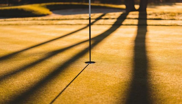 Sunrise golf putting green flagstick casting long diagonal shadows in golden light