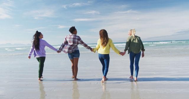 Happy group of diverse female friends having fun, walking along beach holding hands. holiday, freedom and leisure time outdoors.