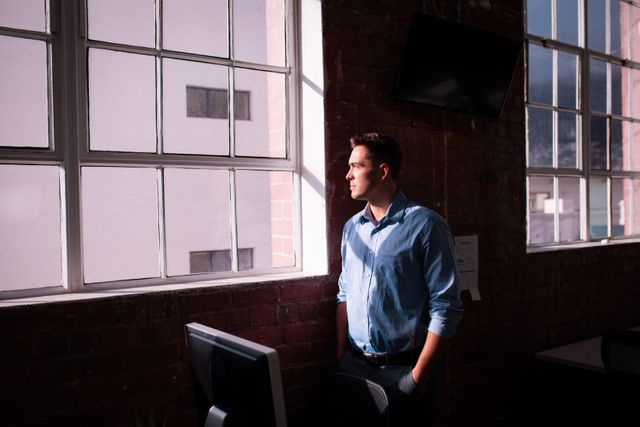 Thoughtful caucasian businessman standing alone in office looking out of window. working in business at a modern office.