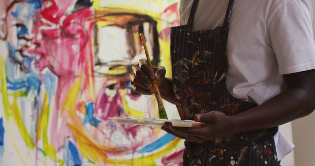 Mid section of african american male artist wearing apron painting on canvas at art studio. art, hobby and creative occupation concept