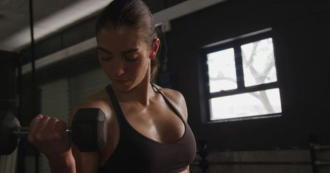 Determined Woman Performing Strength Training with Dumbbell in Modern Gym