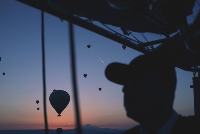 Silhouetted man gazing at hot air balloons floating during sunset. Perfect for travel, adventure, nature, and lifestyle concepts. Ideal for inspiring images of exploration and the beauty of nature, capturing serene evening scenes.