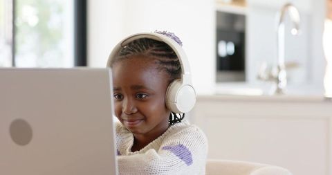 African american girl wearing headphones learning on laptop at sunlit modern kitchen table