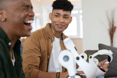 Friends enjoying home vr gaming session on couch with white headset and controllers