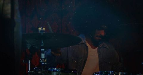 Drummer in denim jacket performing on dimly lit stage