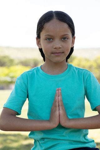 Preteen girl practicing mindfulness prayer pose outdoors in park with calm expression