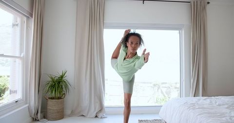 Relaxed Woman Practicing Standing Yoga Pose in Bright Modern Bedroom