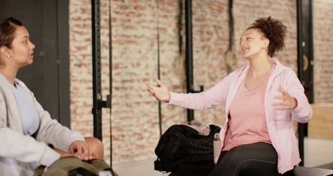 Diverse women chatting after workout in brick-wall fitness studio, relaxing together