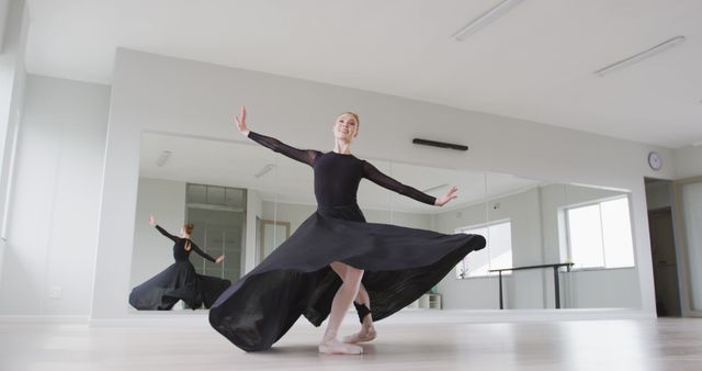 This image shows a ballet dancer spinning gracefully in a dance studio while wearing a black dress and ballet shoes. The background includes mirrors reflecting her movements, enhancing the sense of space and making the dance more captivating. Suitable for use in articles about dance, performing arts, ballet schools, or arts and culture.