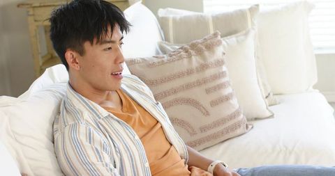 Asian man relaxing on neutral sofa checking smartwatch in bright cozy living room