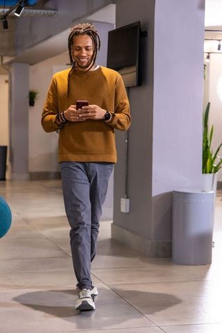 African american man walking, checking smartphone in coworking lobby, mustard sweater