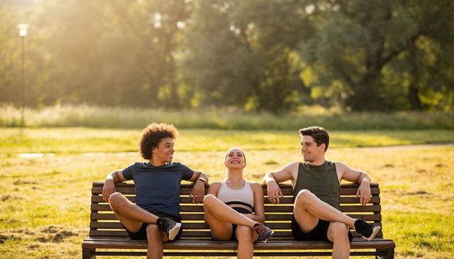 Relaxing trio in athletic wear sitting on park bench at golden hour smiling and chatting