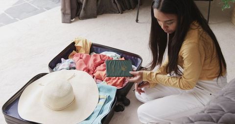 Young woman packing suitcase and holding passport while preparing for summer trip