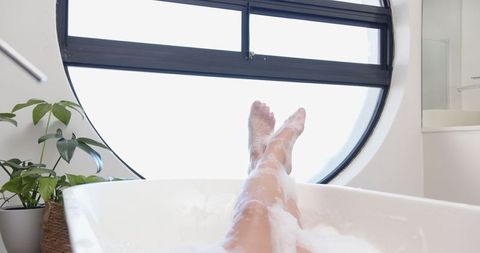 Woman Relaxing in Bathtub with Foam by Round Window