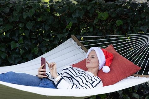 Relaxing christmas at home: middle-aged woman reclining on white hammock wearing santa hat