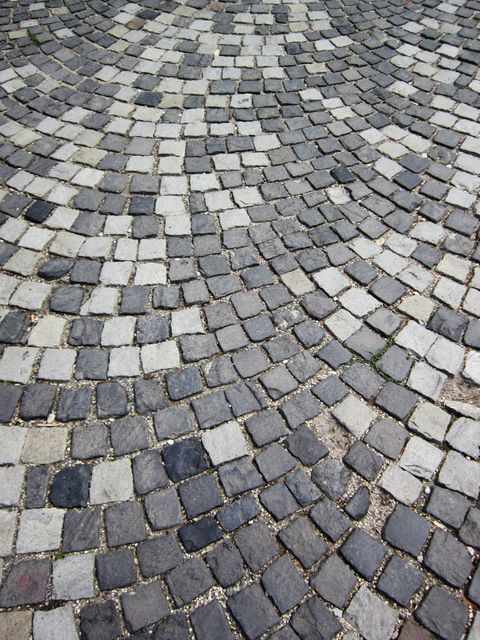Image showcases intricate cobblestone pathway with various shades of grey and white stones arranged in a curved pattern. Ideal for illustrations in historical urban design projects, architectural presentations, and promoting tourism in cities with historical significance.