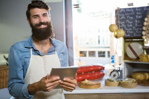 Smiling Shopkeeper Holding Tablet in Artisan Deli Shop