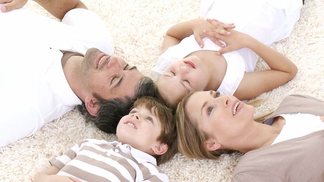 Family lying on a carpet with heads close, creating a sense of unity and togetherness. Suitable for depicting family bonds, domestic life, and leisure time.