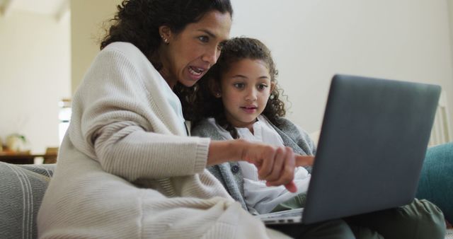 Happy biracial mother and daughter sitting on the sofa,having fun and using laptop. domestic life and family leisure time concept.