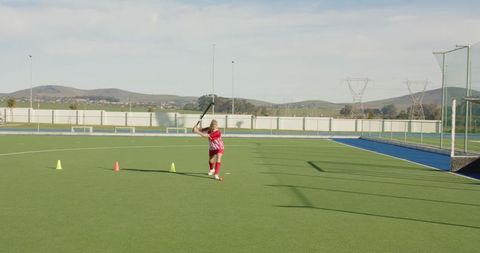 Female hockey player practicing on pitch with focused shot