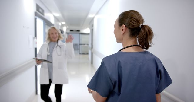 Two healthcare professionals, one appearing as a doctor and the other as a nurse, interacting in a hospital corridor. This scene can be used to depict teamwork and communication in healthcare settings. Ideal for articles and promotions about medical teamwork, hospital environments, or healthcare services.