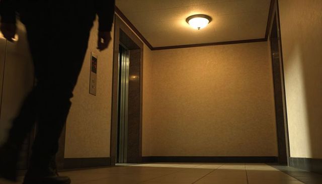 Anonymous silhouette walking past dim elevator lobby under warm ceiling light
