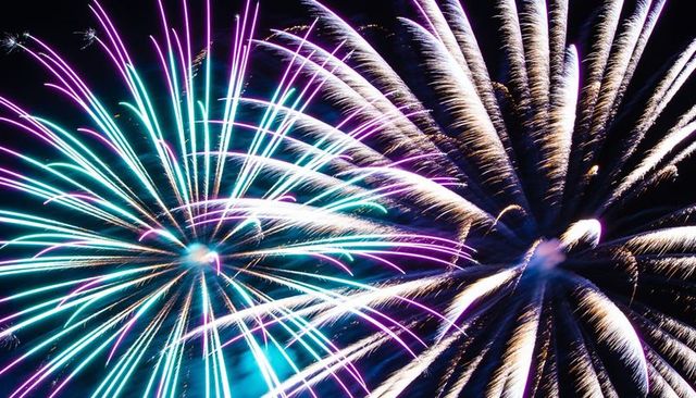 Vibrant teal purple fireworks bursting against dark sky with white-gold spark trails