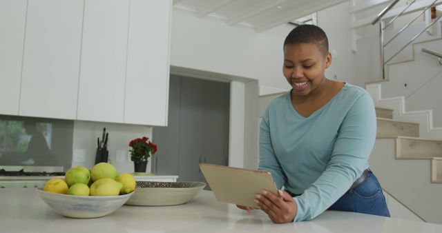Happy african american plus size woman using tablet in kitchen. domestic lifestyle, enjoying leisure time at home with technology.