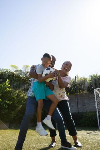 Cheerful Family Lifting Son with Soccer Ball In Sunny Yard