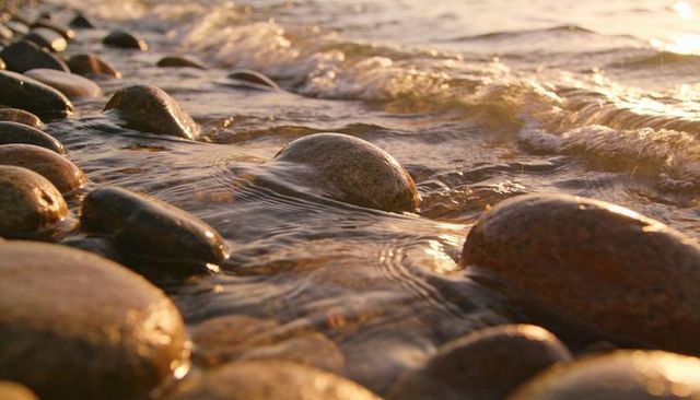 Golden sunset light reflecting on smooth wet pebble beach with gentle wave motion