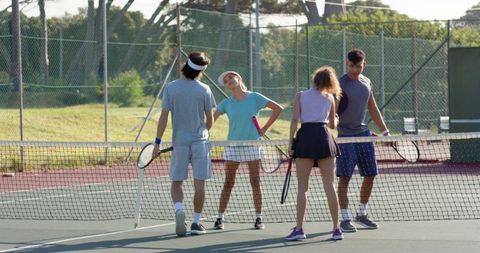 Multicultural players chatting at tennis net on sunny hard court doubles casual
