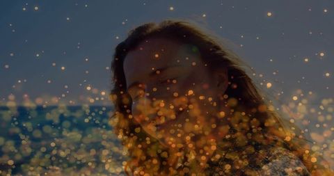 Gazing woman at sea with golden bokeh lights during sunset backlight portrait