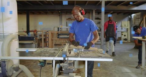 Carpenter cutting hardwood on table saw while wearing safety goggles and ear protection
