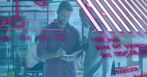 Developers collaborating over notebook while writing code on glass wall in open office