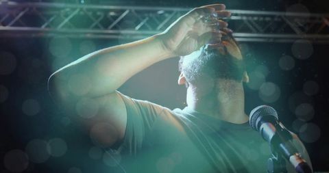 Performer taking shot on stage under spotlight with microphone, bokeh lights and haze