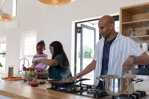 African american family cooking together in bright modern kitchen, father stirring pot