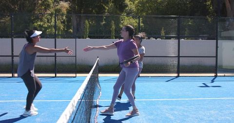 Women reaching across net for post-match handshake on blue outdoor pickleball court