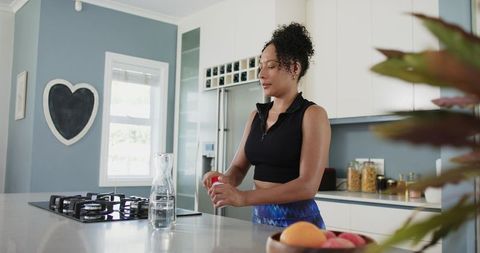 African american woman making breakfast in modern kitchen pouring water from carafe