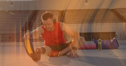 Determined amputee athlete stretching on outdoor track with prosthetic blade and headphones