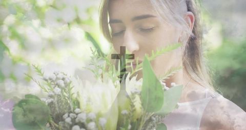 Serene young woman smelling bouquet with cross overlay double exposure conveying faith and peace
