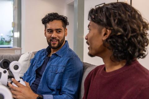 Diverse men testing wireless headset while talking on couch, tech conversation