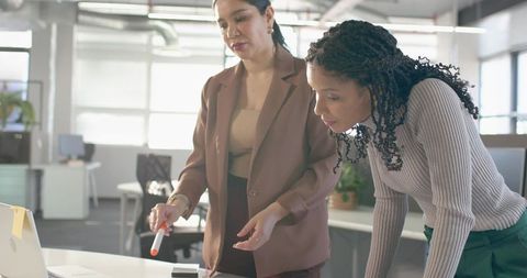 Two businesswomen collaborating over laptop in bright modern open-plan office for teamwork