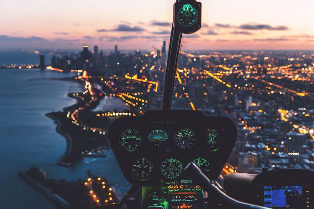 Aerial view of a brightly lit city at night from inside a helicopter cockpit. City skyline illuminated against the dusk sky, showcasing landmark buildings and urban lights twinkling below. Ideal for use in themes that involve urban exploration, night flights, aviation technology, city living, or transportation.