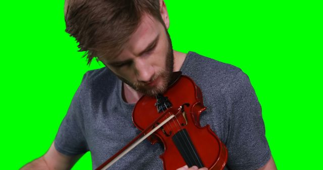 This image depicts a man focusing intently while playing a violin with a green screen background. Ideal for music-related themes, promotional materials for musicians, or projects requiring isolated subjects to place over custom backdrops. The green screen makes it easy to insert different backgrounds for various creative needs.