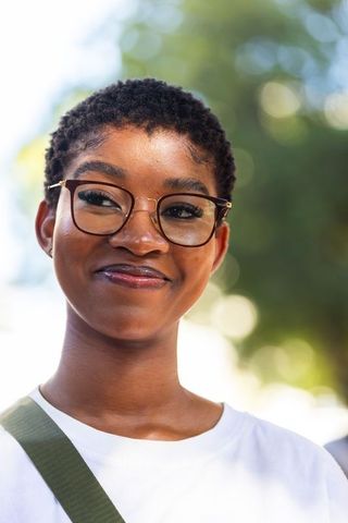 Confident african woman wearing glasses, short hair and white t-shirt smiling outdoors with olive gr