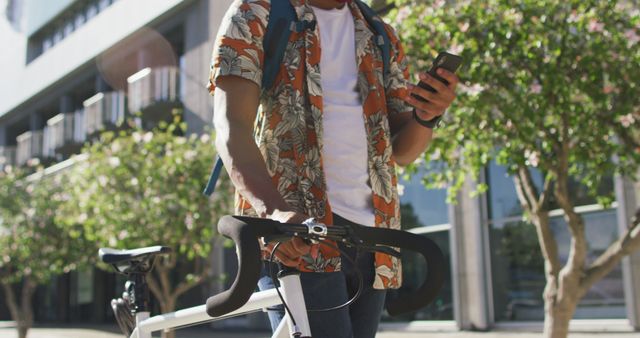 Man standing on urban street holding smartphone and bicycle. Ideal for use in marketing campaigns for mobile technology, transportation options, urban lifestyle promotions, and casual fashion advertisments.