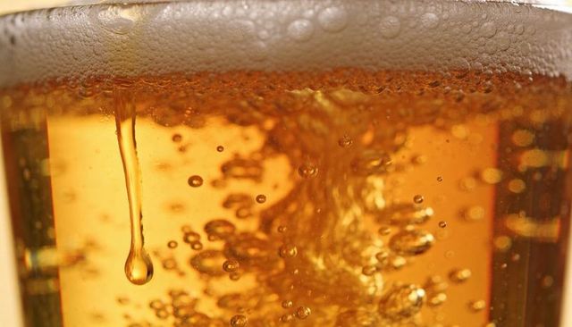 Macro showing amber beer with rising bubbles, creamy foam and hanging droplet