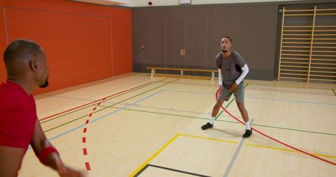 Diverse male teammates passing basketball on indoor gym court practicing teamwork and fitness drills