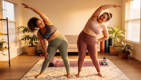 Two Women Doing Side Stretches in Sunlit Living Room During Home Workout