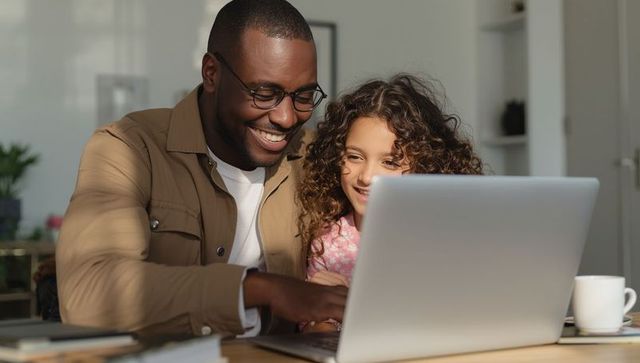 Father and Daughter Smiling at Laptop in Home Dining Area